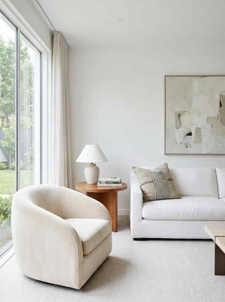  White living room with one sculptural curved accent chair in soft velvet placed at an angle near a white sofa