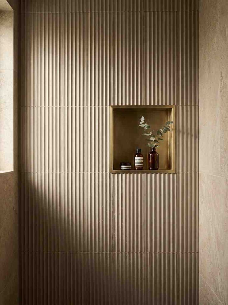 20 Bathroom Ideas 2026 A close-up editorial photograph of a bathroom shower wall covered in vertical fluted ceramic tiles in a warm greige tone.